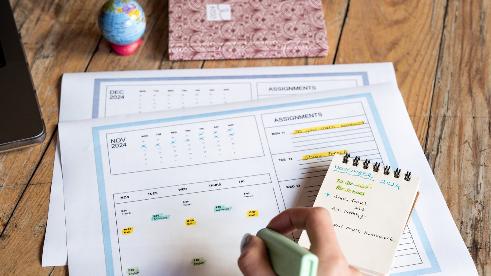 A hand marking plans on a paper calendar beside a notebook